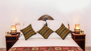 Un lit bien fait, agrémenté d’oreillers à rayures et d’une couvre-lit à motifs rouges. Deux tables de chevet, chacune surmontée d’une lampe, se trouvent de part et d’autre du lit.