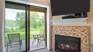 Una habitación con chimenea, televisor montado encima y puerta corrediza de vidrio que da a un patio exterior con sillas.