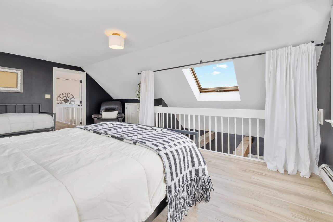 Un dormitorio con cama, tragaluz, barandilla blanca y vista al cielo.