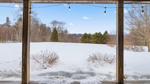 A wooden deck with a view of a snowy landscape and trees. - "Big Sky" Retreat Atop Sunapee with Overflow Unit (Newbury)