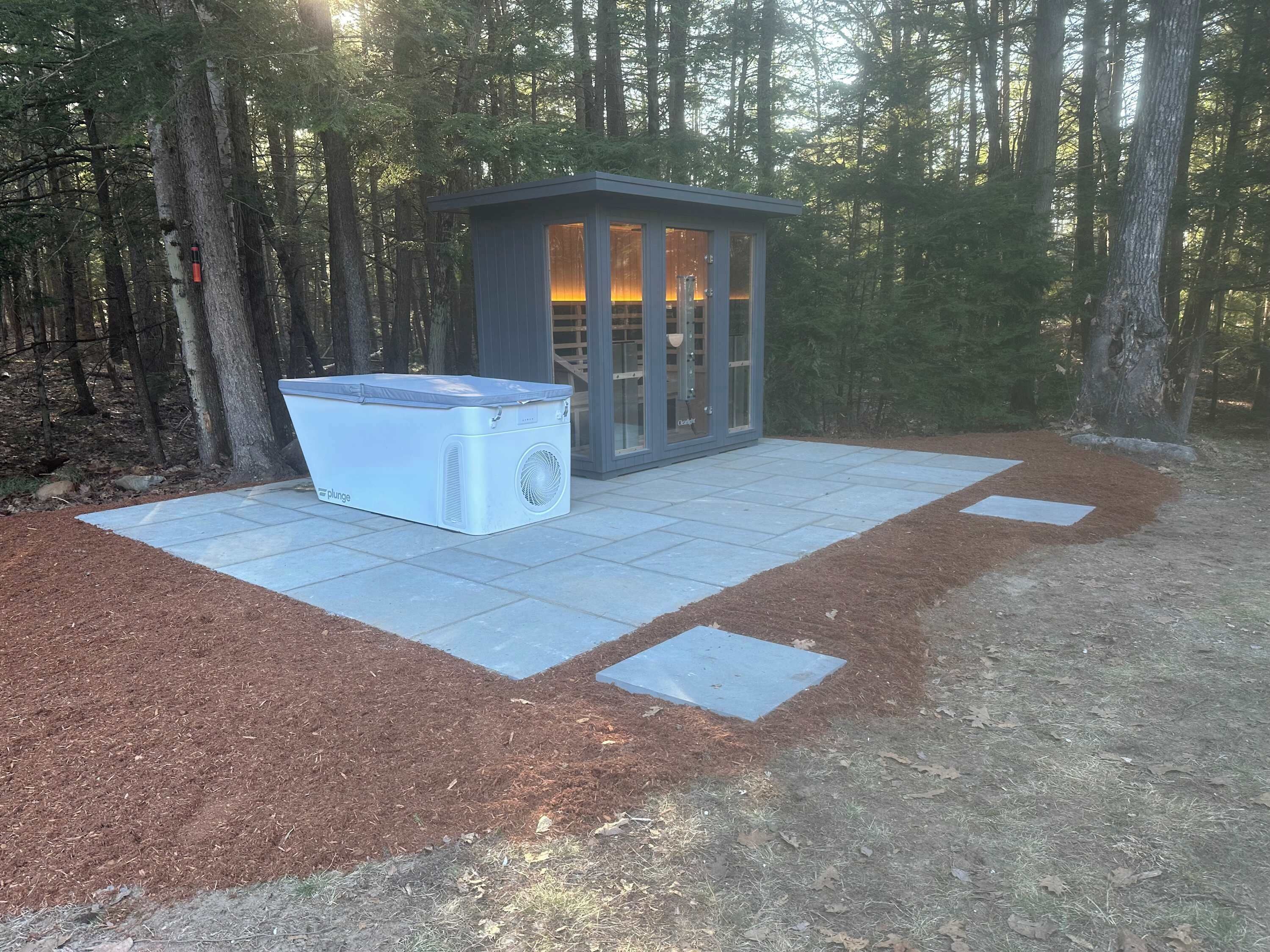 A small outdoor sauna with a glass enclosure and a large portable sauna unit beside it.