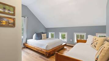 A bedroom with a sloped ceiling, a wooden bed frame, a white bed, and two windows with curtains.