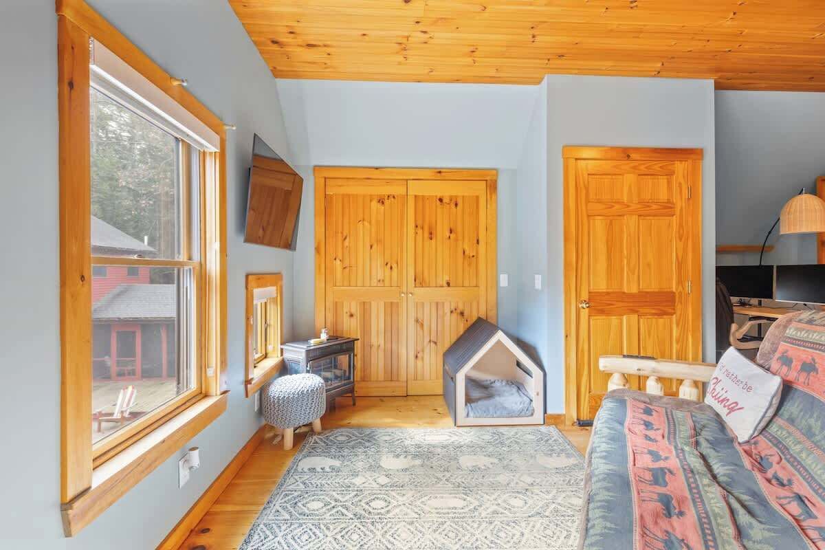 Una habitación acogedora con un ventanal grande, puertas de madera, una cama en forma de casa pequeña, un tapete estampado y un sofá con cojines decorativos.