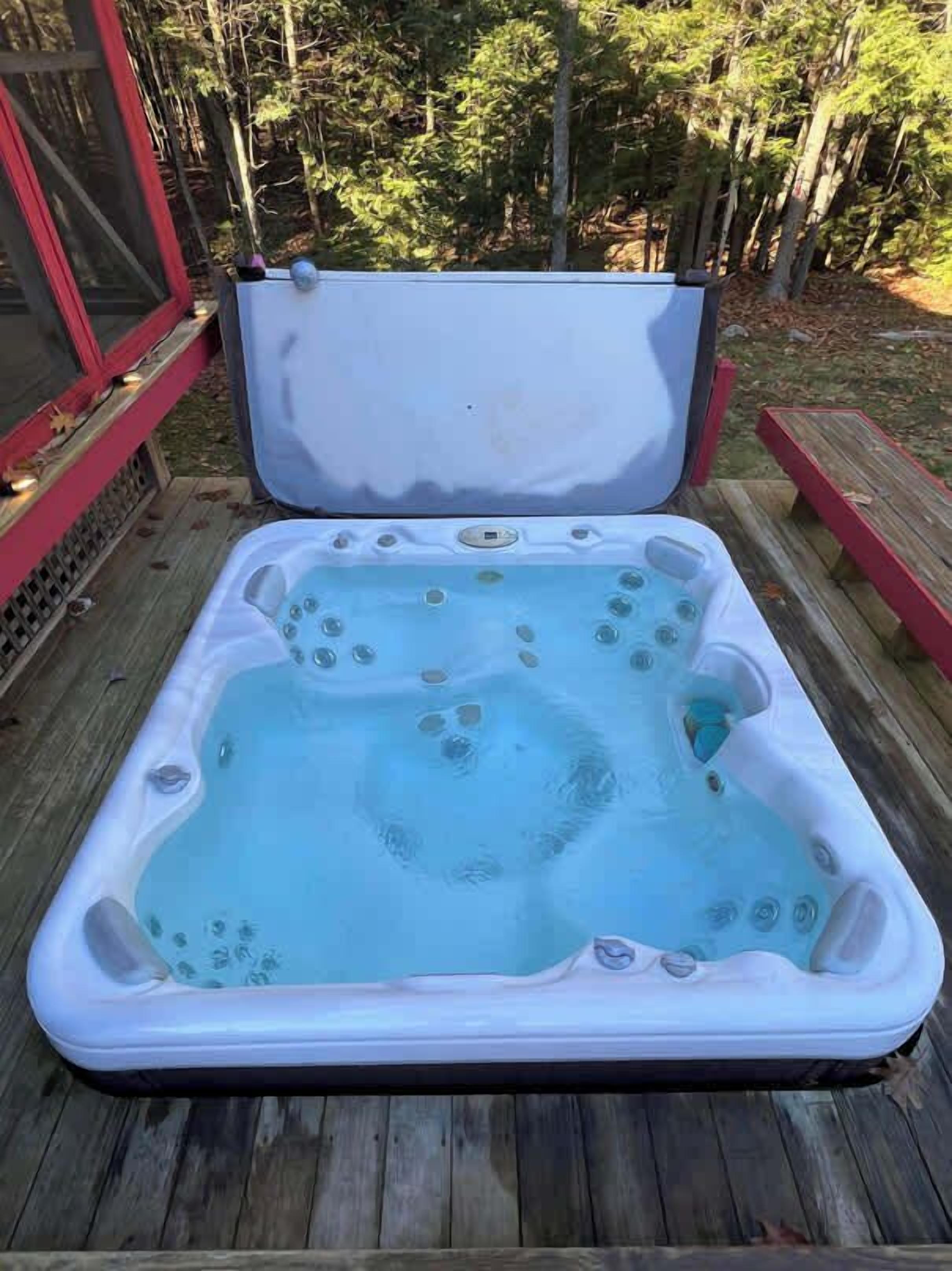 Ein Whirlpool auf einer Holzterrasse, umgeben von Bäumen.