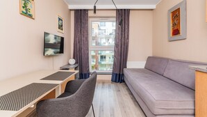 A modern living room with a sofa, a TV, a desk, and a window with curtains.