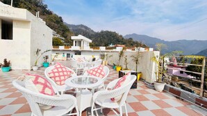 Eine Terrasse mit weißen Korbmöbeln und Blumentöpfen mit Blick auf eine gebirgige Landschaft.