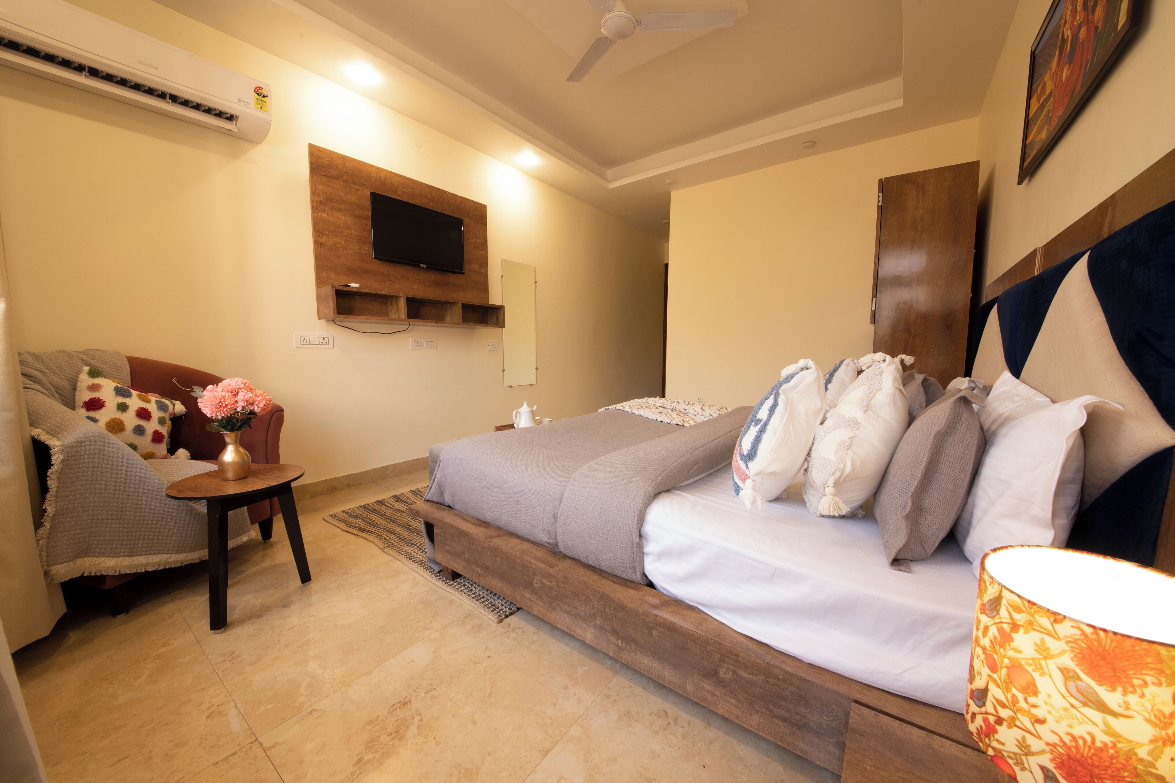 A bedroom with a bed, a sofa, a TV mounted on the wall, and an air conditioner.