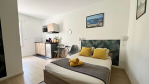 Une chambre moderne avec un lit, un petit bureau et un coin cuisine.
