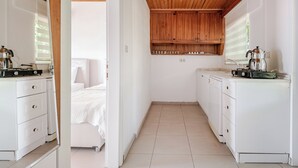 Cocina compacta y moderna con armarios blancos, techo de madera y una ventana pequeña.