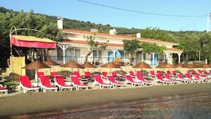 Un hotel frente a la playa con filas de tumbonas rojas y blancas, sombrillas y una vista despejada del mar.
