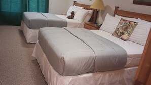 A hotel room with two beds, each with a pillow and a blanket. There is a nightstand with a lamp and a teddy bear on one of the beds. - Cozy 1-bedroom condo in charming Driggs with WiFi (Driggs)
