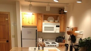 A modern kitchen with wooden cabinets, a central island with stools, a microwave, stove, and a refrigerator. - Cozy 1-bedroom condo in charming Driggs with WiFi (Driggs)