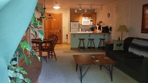 Un salon confortable avec une table à manger, un canapé et un coin cuisine équipé d’un four à micro-ondes et de tabourets.