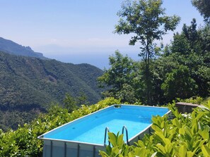 An outdoor swimming pool surrounded by lush greenery and overlooking a mountainous landscape. - Entire Villa (Ravello)