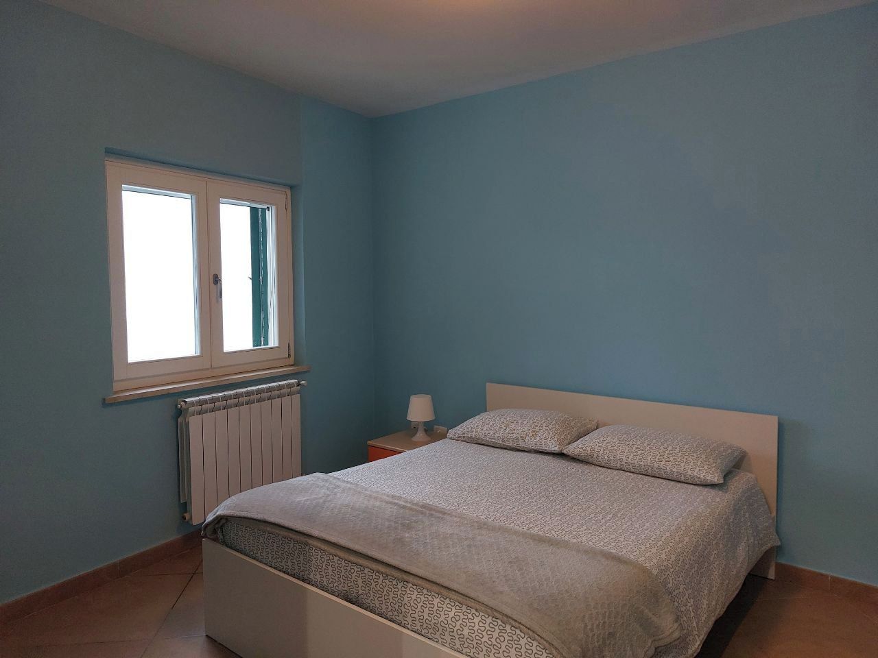 Een slaapkamer met een bed, een raam, een nachtkastje en een lamp.