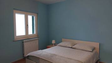Een slaapkamer met een bed, een raam, een nachtkastje en een lamp.