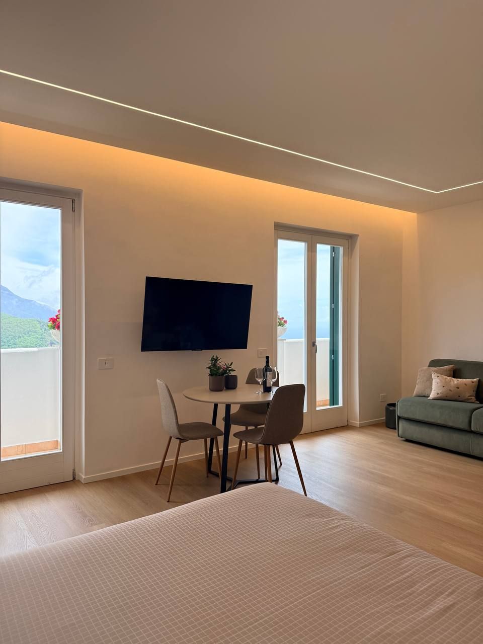 Een moderne kamer met een bed, een eettafel met stoelen, een flatscreen televisie aan de muur en een balkon met uitzicht.