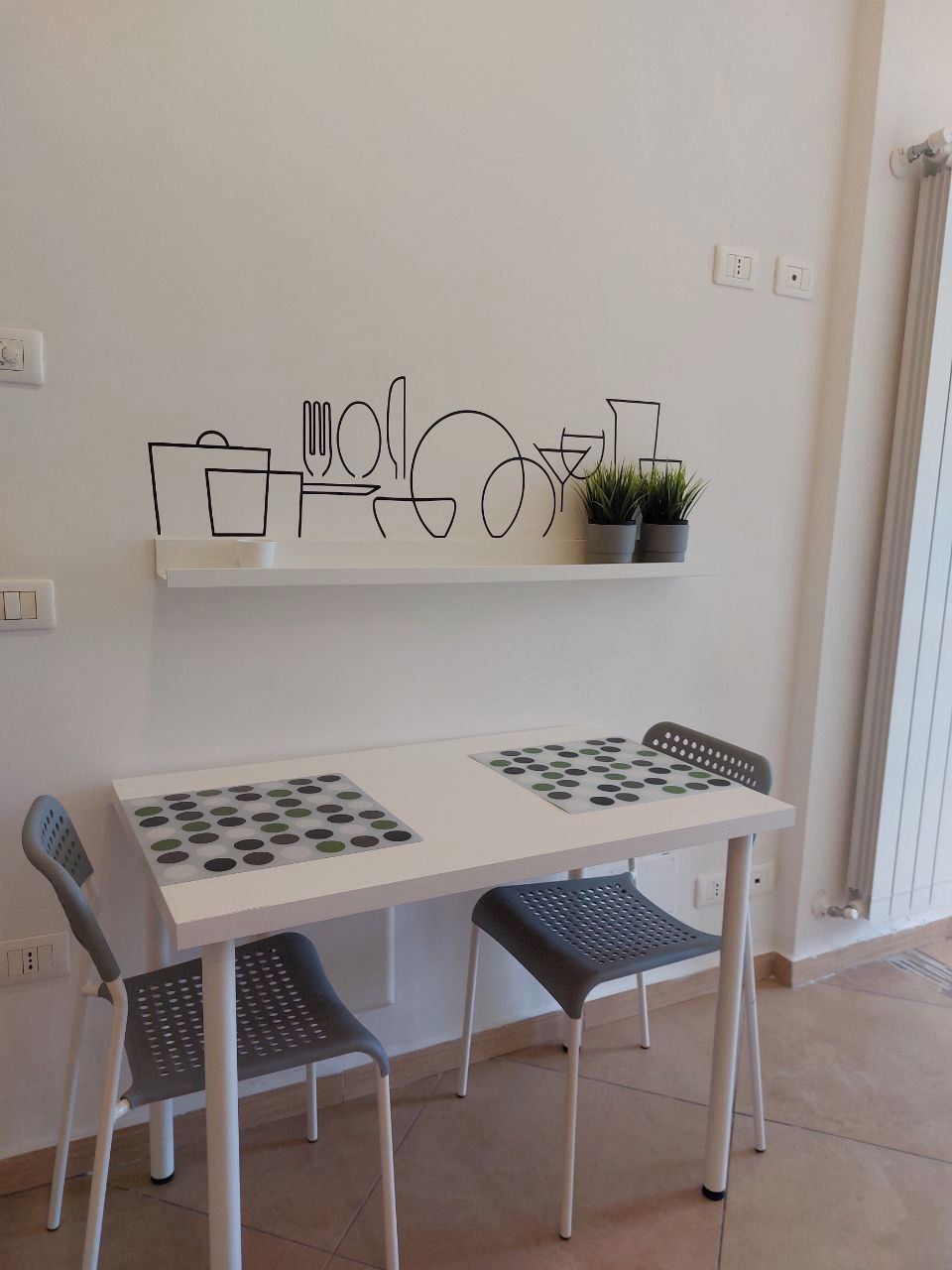 Un tavolo bianco con due sedie, uno scaffale a parete con un'opera d'arte minimalista e una pianta in vaso.