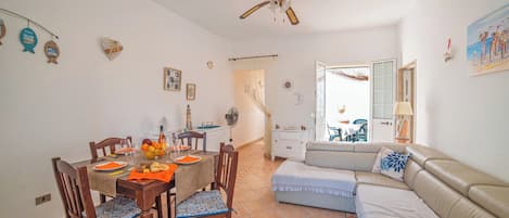 Un comedor con una mesa preparada para cuatro personas, un sofá y un ventilador de techo.