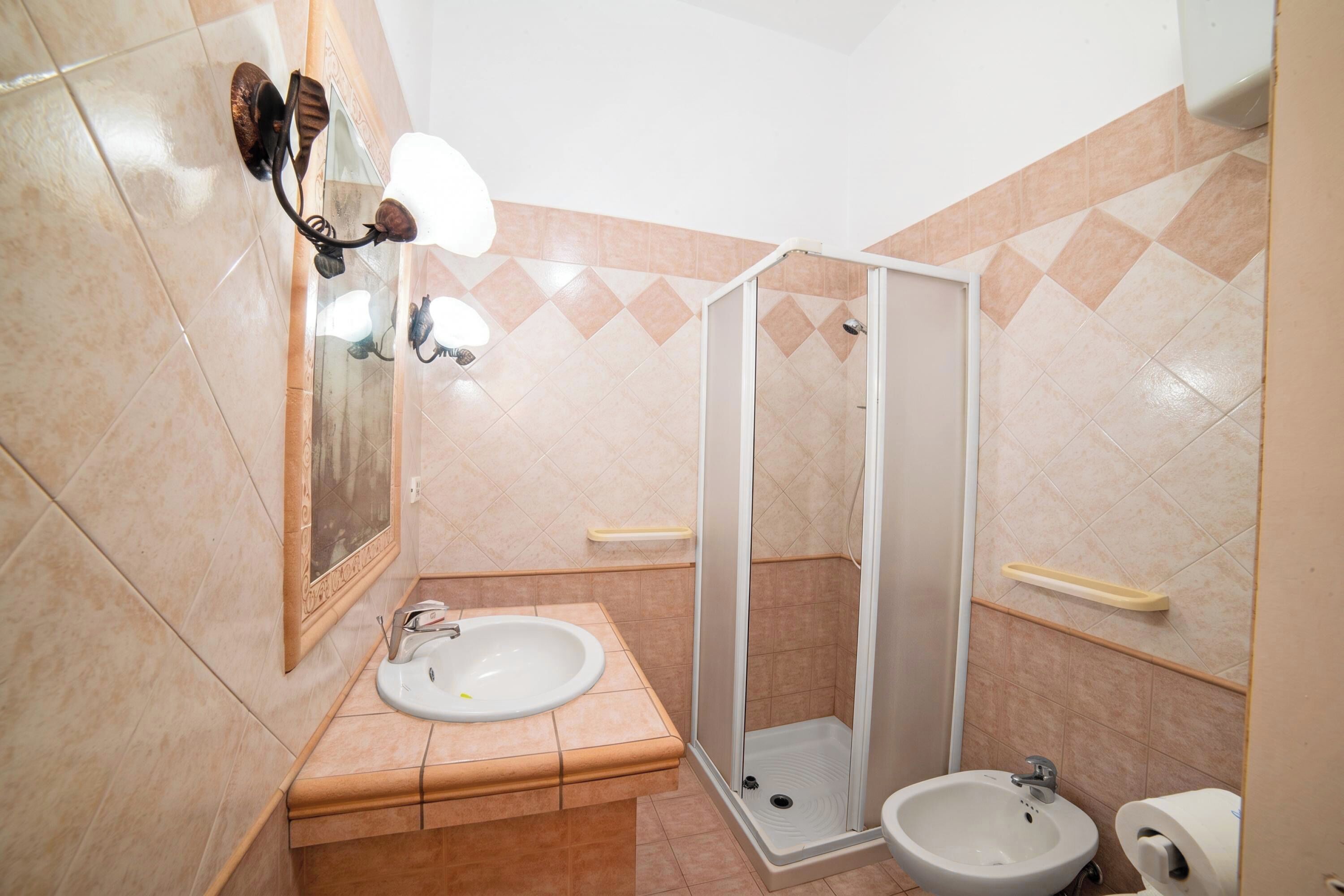 A bathroom with a sink, a bidet, a shower enclosure, and a mirror with wall-mounted lights.