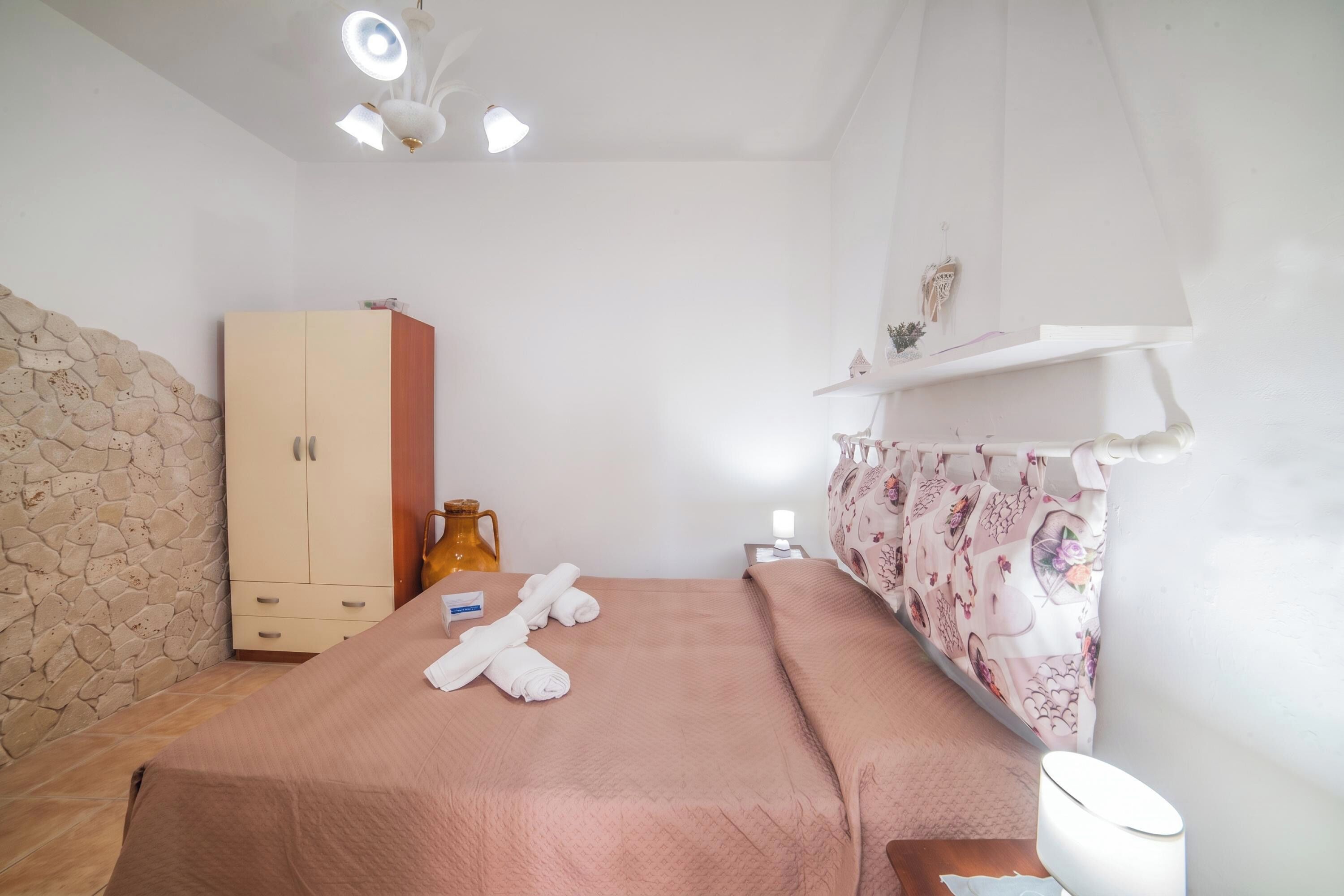 A bedroom with a bed, a wardrobe, a nightstand, a lamp, and a decorative wall.