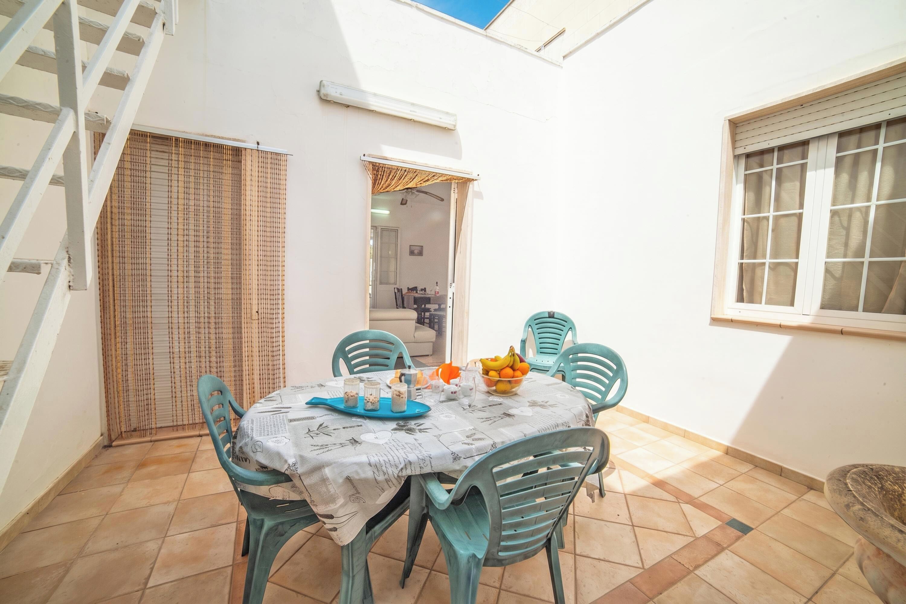 A small dining area with a table set for two, surrounded by chairs, a window with blinds, and a door leading to another room.