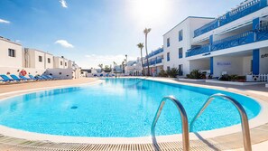 A swimming pool with sunbathing loungers and a building labeled 'BELLISIMA' in the background.