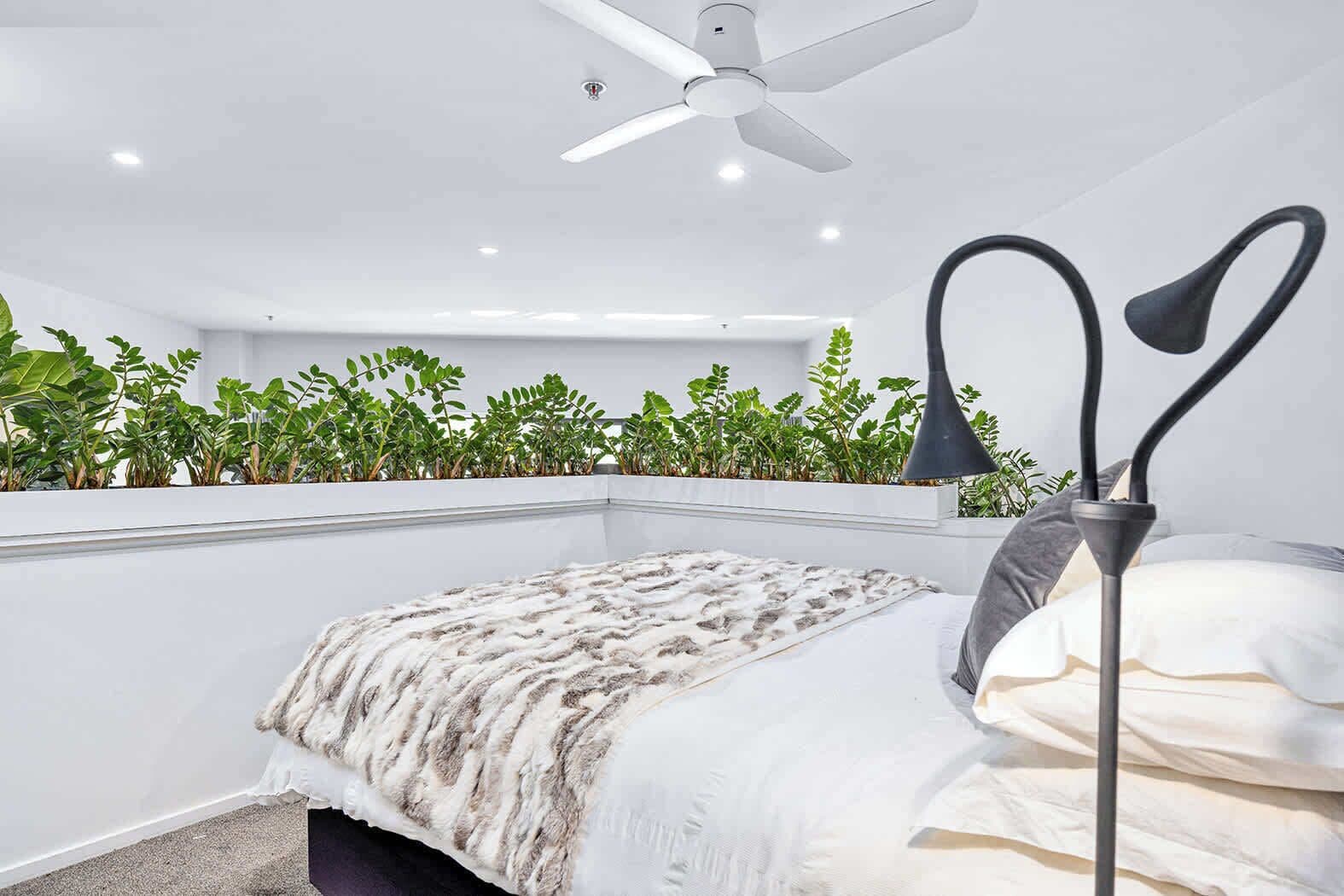 A bedroom with a bed, a ceiling fan, a bedside lamp, and a plant wall.