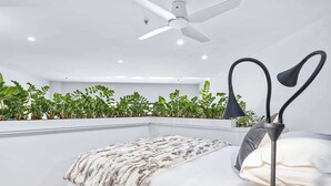 A bedroom with a bed, a ceiling fan, a bedside lamp, and a plant wall.