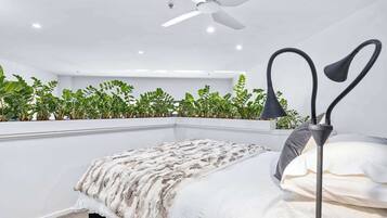 A bedroom with a bed, a ceiling fan, a bedside lamp, and a plant wall.