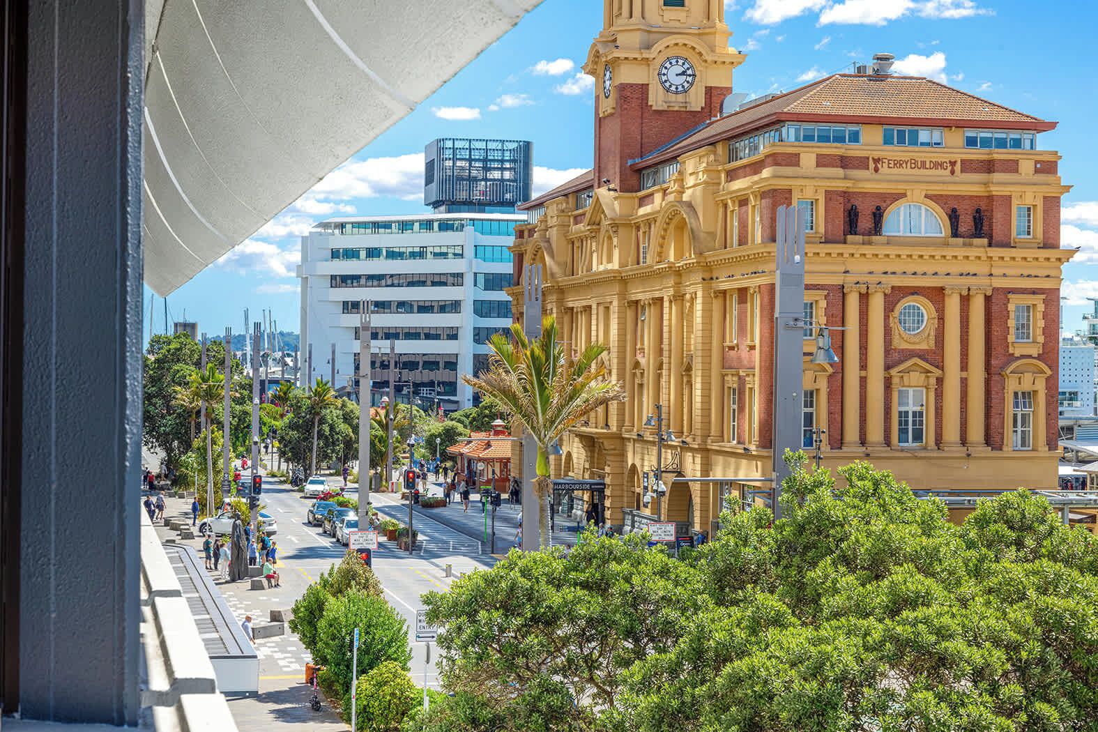 A historic building with a clock tower, a modern adjacent building, and a busy street with pedestrians and vehicles.