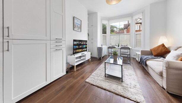 Een moderne woonkamer met witte kasten, een flatscreen-tv, een glazen salontafel en een beige bank.