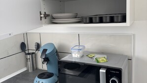 A compact kitchen with a coffee machine, a microwave, and a shelf with glassware and plates.