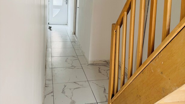 A hallway with marble flooring, white walls, and a wooden staircase.