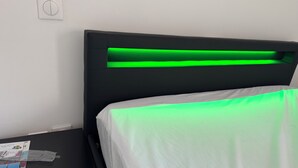 A bed with a white sheet and a black headboard with green underlighting.