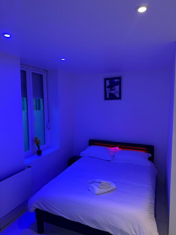 A bedroom with a bed, a window with blinds, a wall-mounted picture, and a ceiling light.