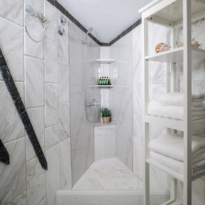 A bathroom with a shower, a sink, a shelf with toiletries, and a towel rack. - Casa della Liberta Firostefani (Santorini)