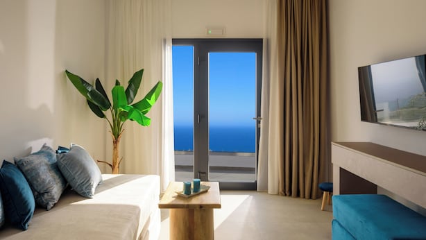 A modern living room with a sofa, a coffee table, and a TV. There is a large window with a view of the ocean. - Casa della Liberta Firostefani (Santorini)