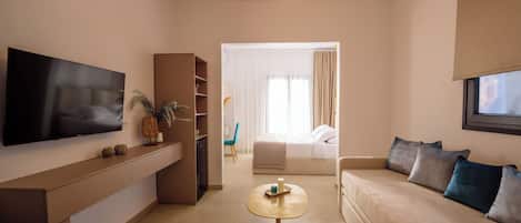 A modern hotel room with a flat-screen TV, a sofa, a small round table, a bed, and a large window with curtains.