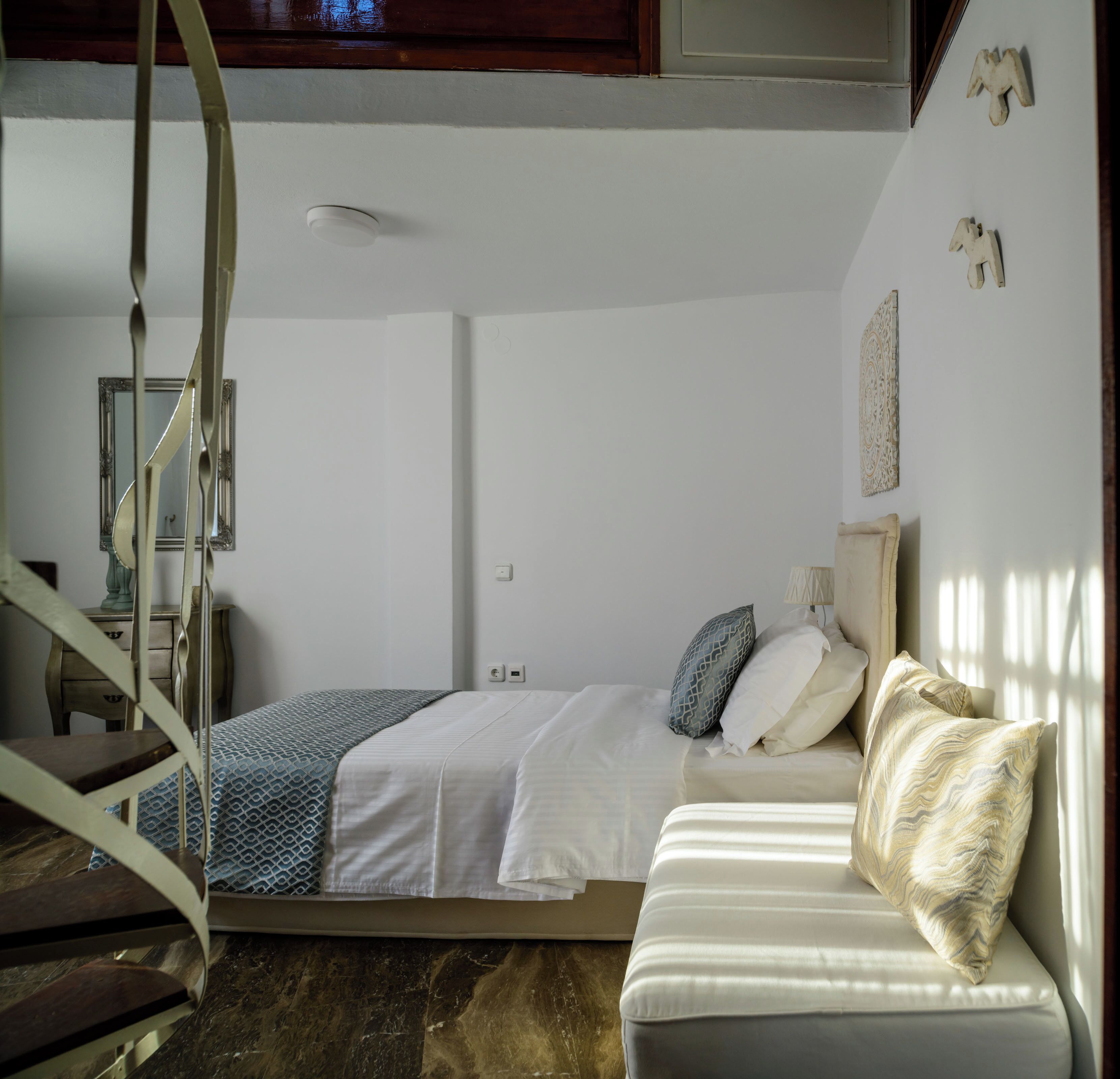 A bedroom with a bed, a chair, a bedside table, and a wall-mounted light fixture.