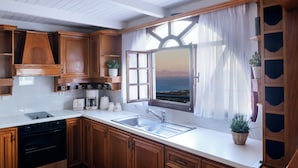 A kitchen with wooden cabinets, a built-in oven, a sink, and a window with a view of the sea. - Casa della Liberta Firostefani (Santorini)