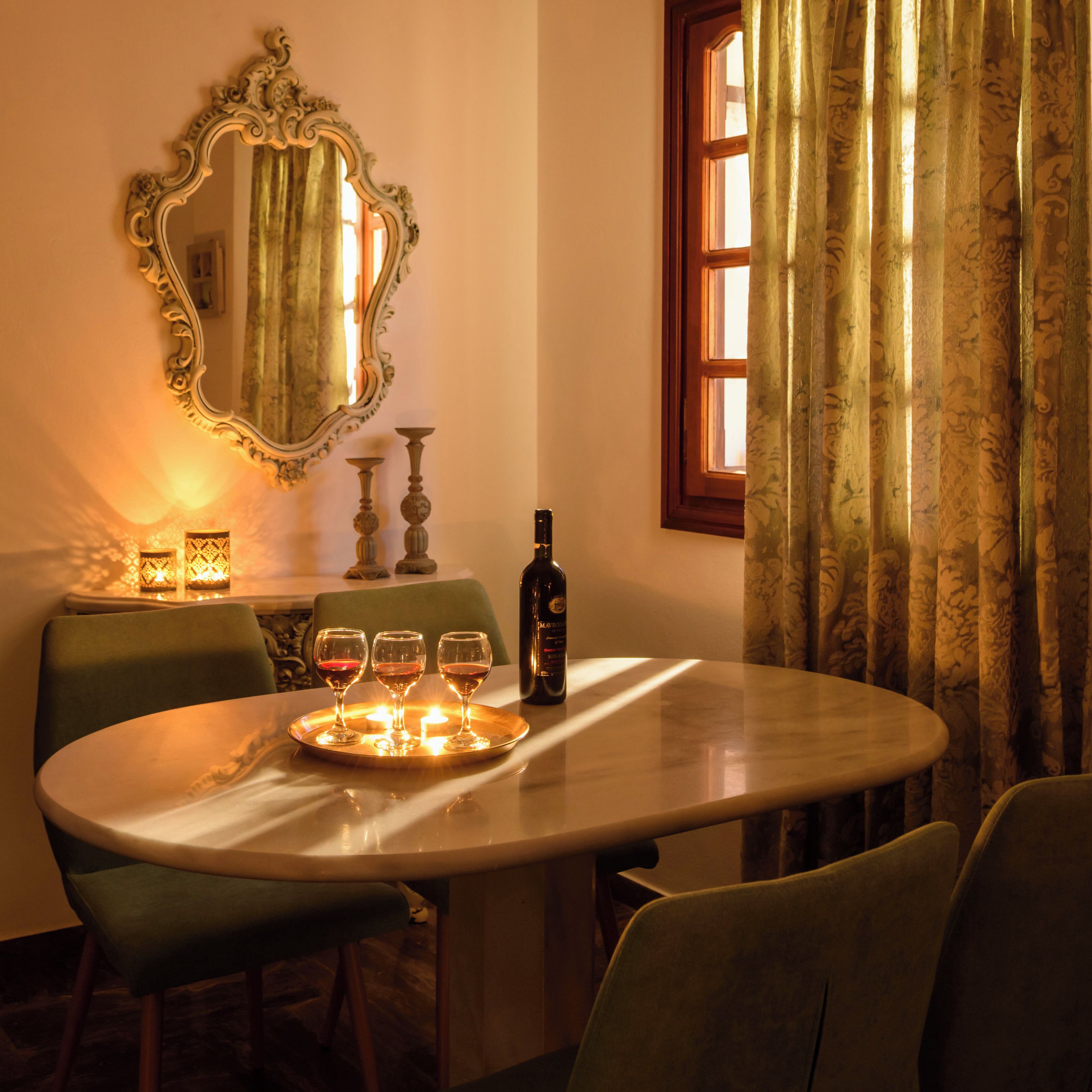 A dining table with three wine glasses, a bottle, and candles.