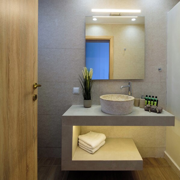 A modern bathroom with a wooden door, a round sink, a mirror, and a shelf with towels. - Casa della Liberta Firostefani (Santorini)