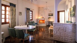 A dining area with a round table, chairs, a fireplace, and a stone wall. - Casa della Liberta Firostefani (Santorini)
