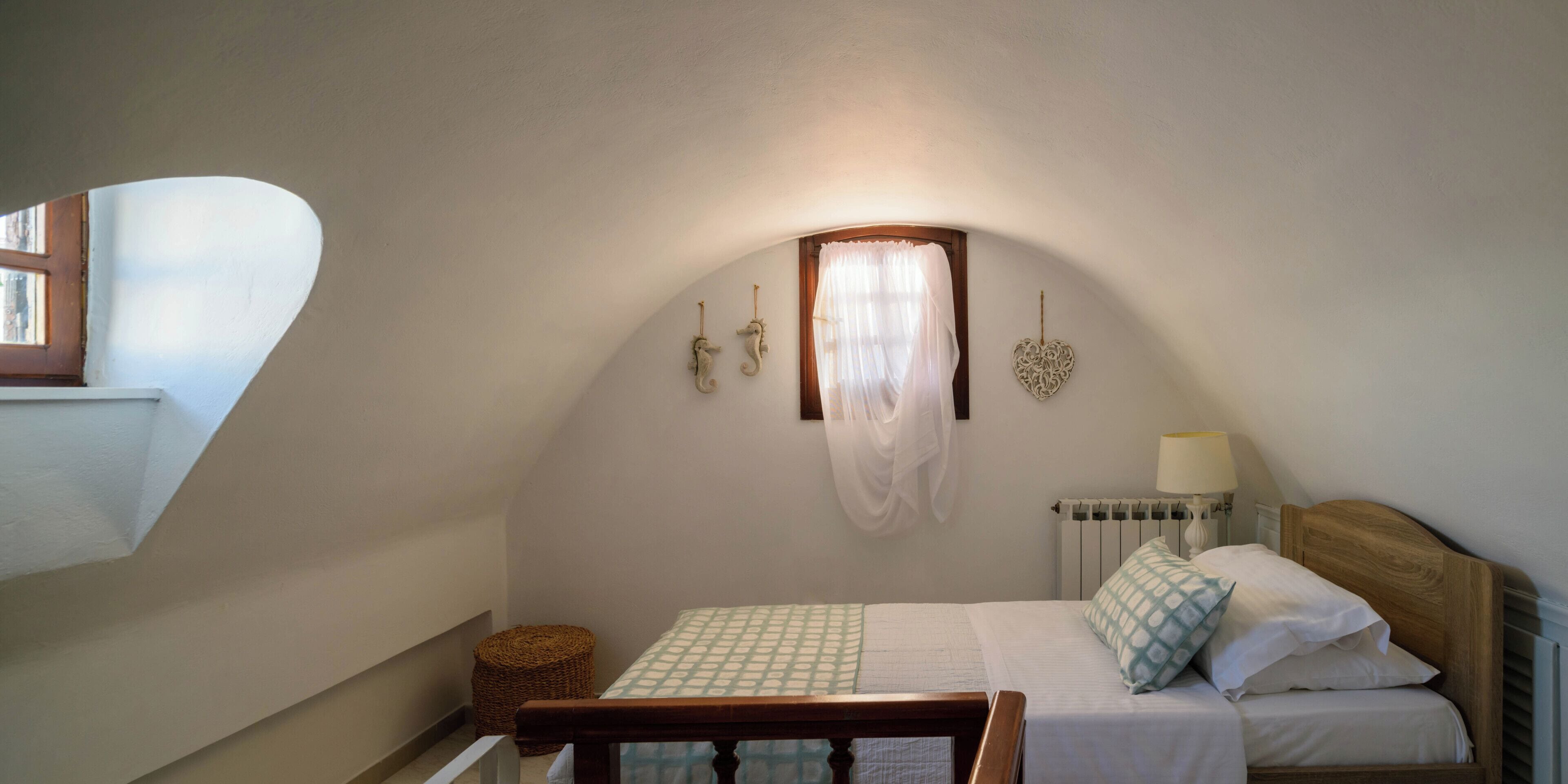 A bedroom with a sloped ceiling, a bed with a wooden headboard, a bedside table with a lamp, and a wall-mounted decorative item.