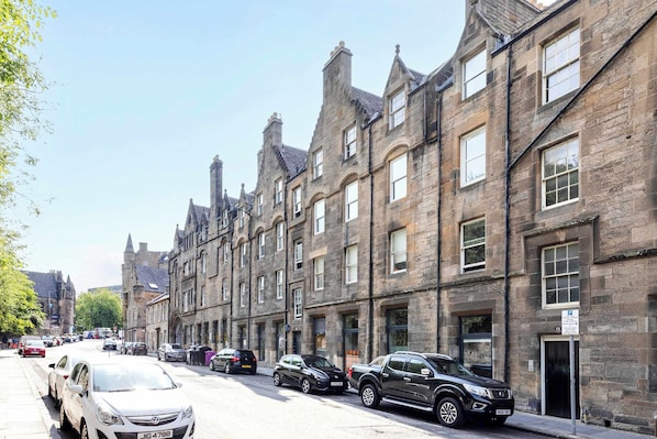 A row of historic stone buildings with parked cars on the street.