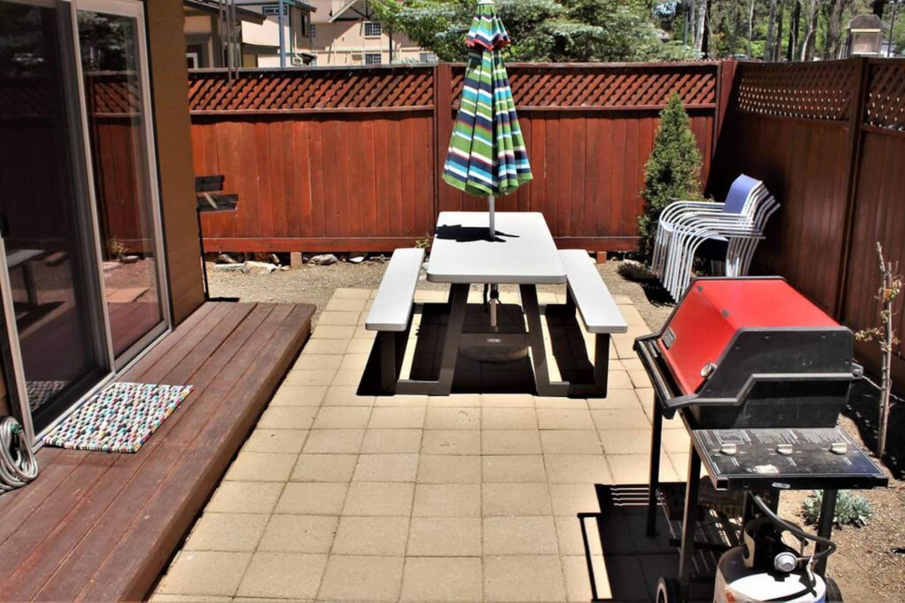 Un jardin avec une table de pique-nique, un barbecue et un parasol à rayures.