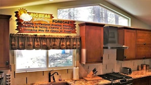 Una cocina con armarios de madera, encimera de granito, pileta de acero inoxidable, estufa y ventana con vista a un paisaje nevado.