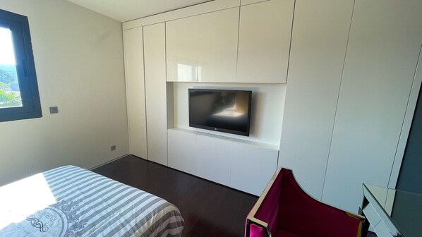 Un dormitorio con una cama, un televisor montado en la pared y una ventana.