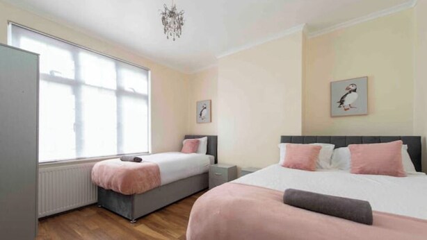 A bedroom with two beds, a radiator, a window, and a chandelier. - Sleeps 10 few minutes' walk to Abbeywood Station (Gillingham)